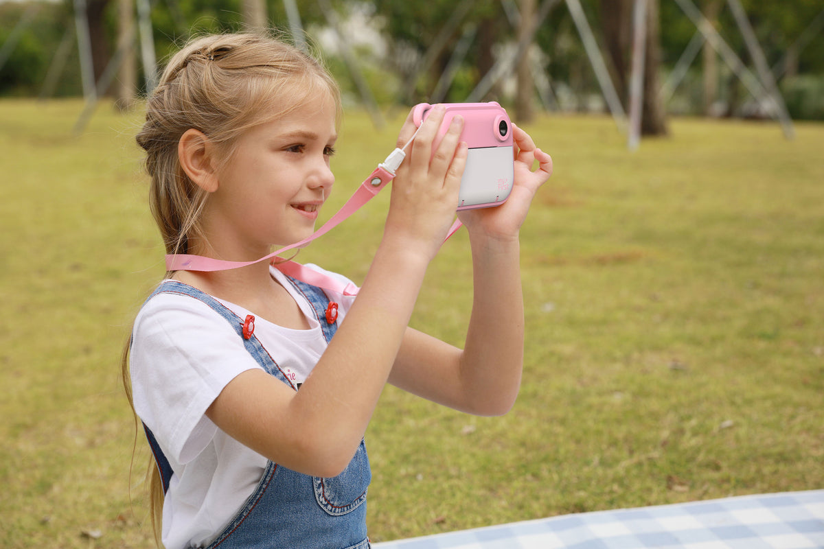 Young girl holding a pink toy camera in an outdoor setting